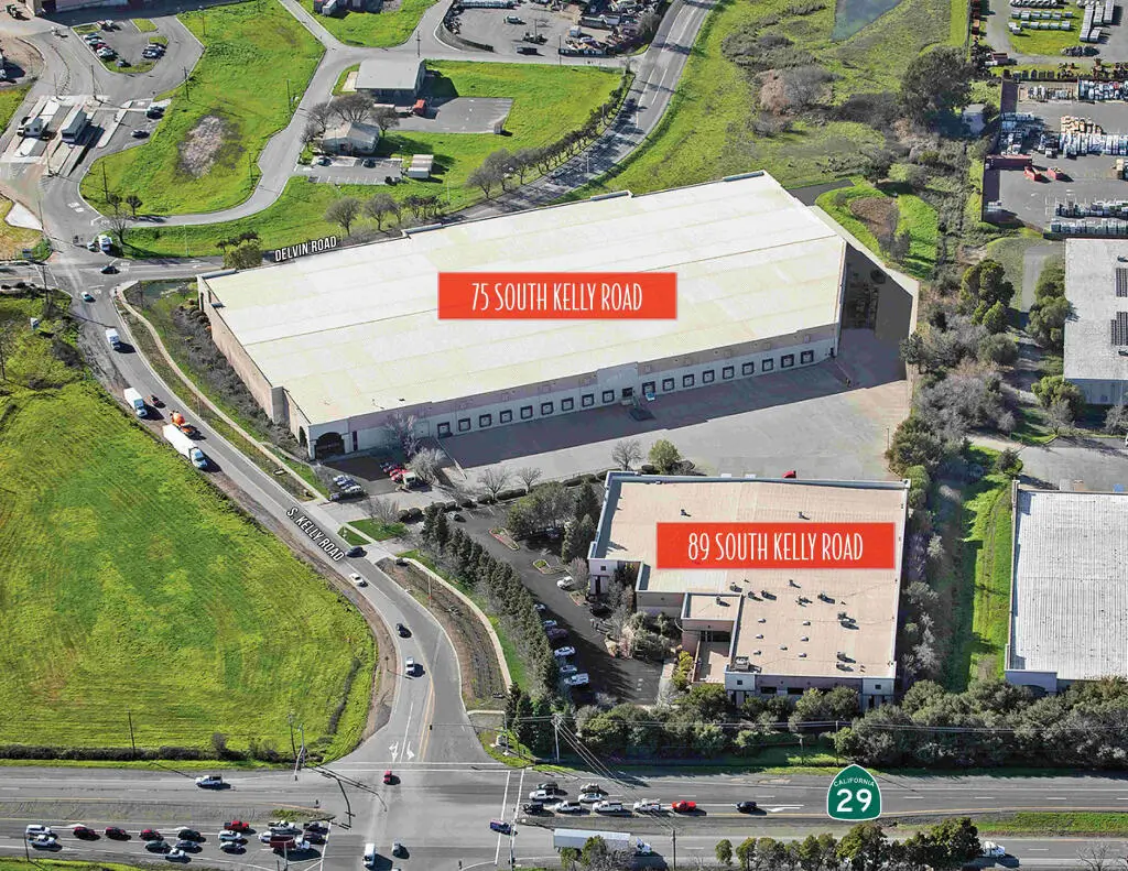 Aerial view of  a two warehouse in Napa Valley with cars on the road and a wide range of grass field.